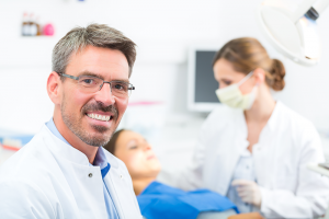 Male dentist smiling with patients in the background