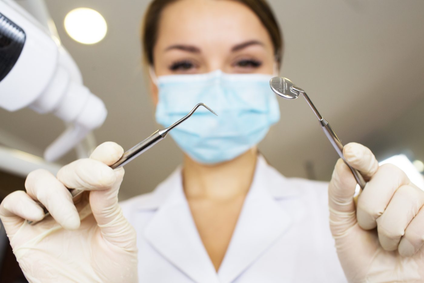 young women dentist with sterile mask readily approaching a patient with dental instruments held in the hands protected with surgical gloves young dentist with sterile mask.Dentist